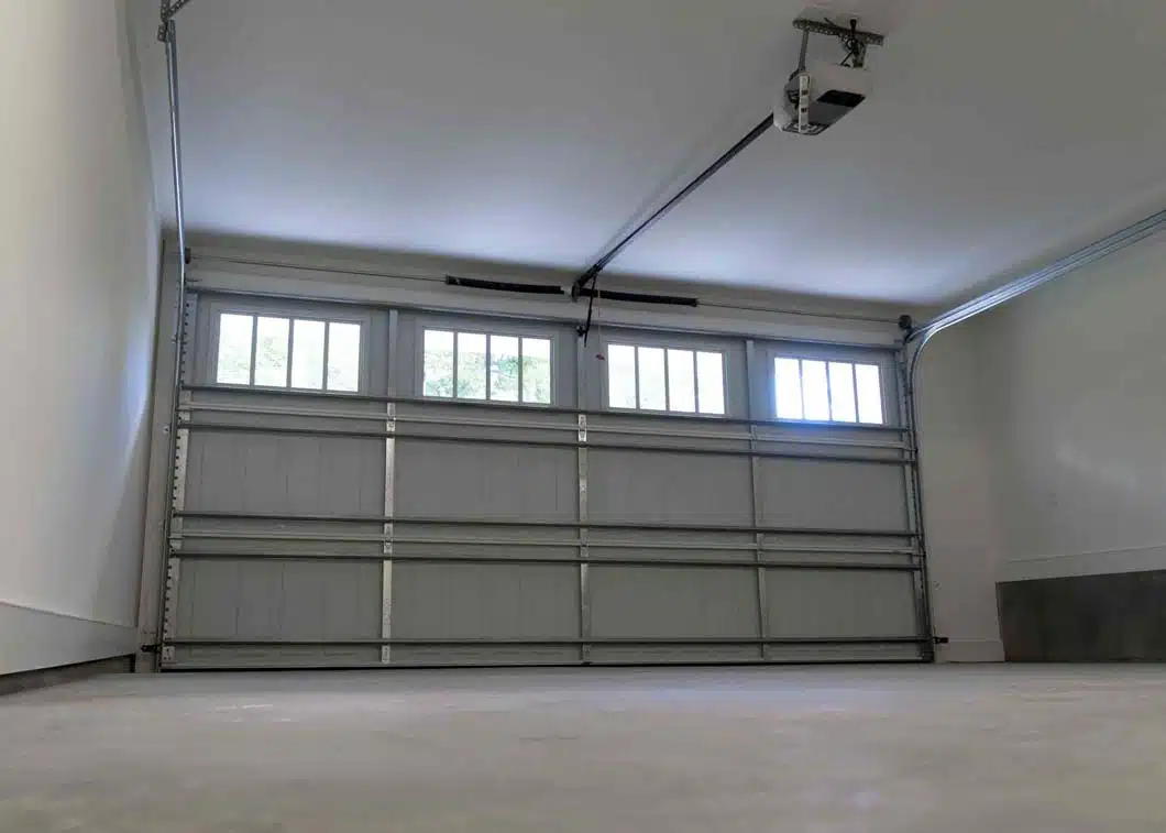 Interior view of a closed sectional garage door with upper row windows and door opener in a clean, well-lit garage